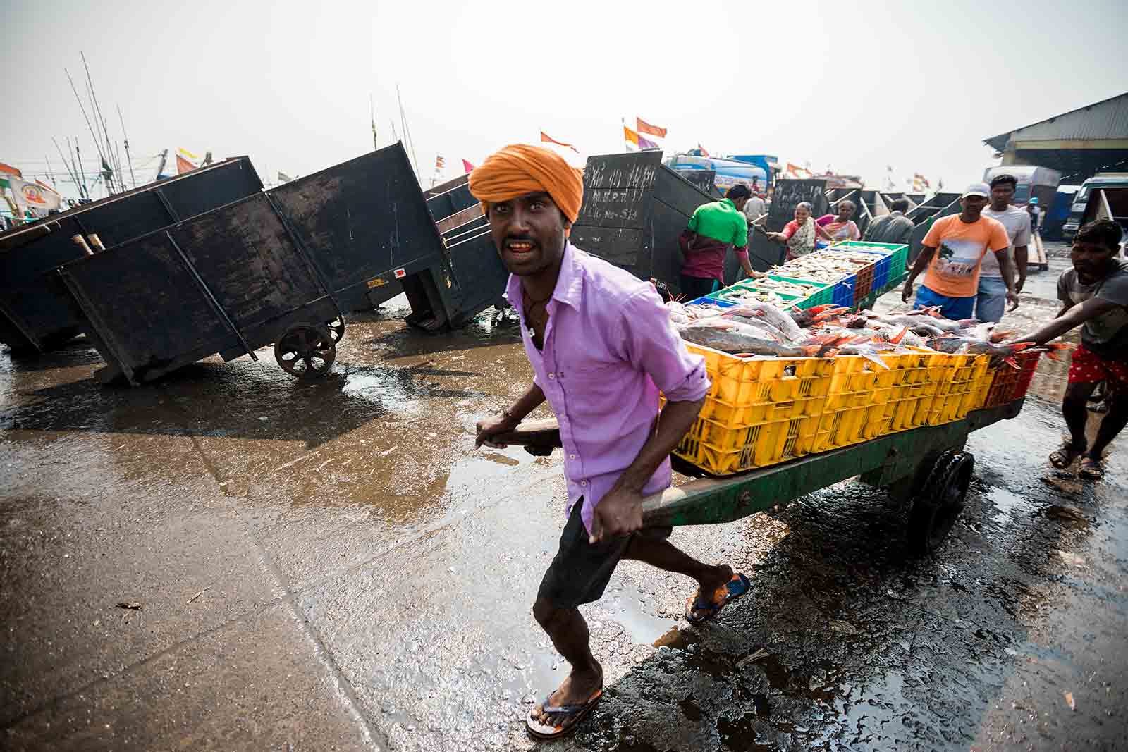 Men push loaded handcarts through the crowds at Sassoon Docks as they yell for people to get out of the way.
