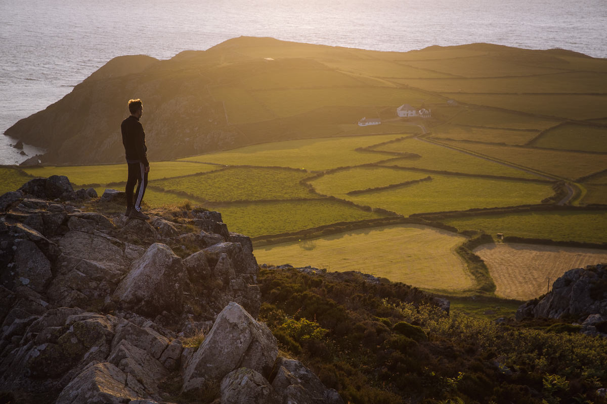 man stands on a rock overlooking a patchwork of fields by the sea