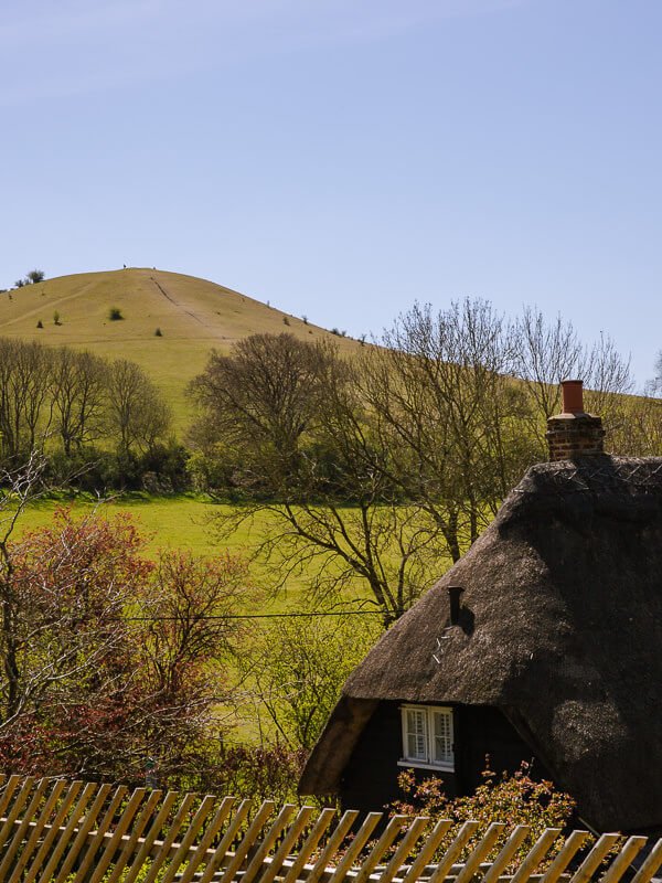 A thatched roof cottage under a green hill on the lovely Coombe Hill walk near London