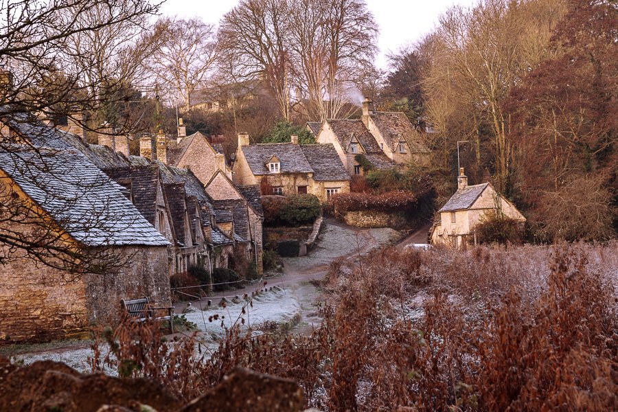 A row of slate roof weaver cottages through trees covered with frost Cotswold Villages