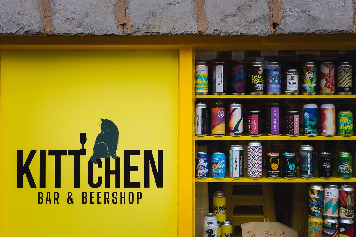 Colourful craft beer cans stacked up in a window with KITTCHEN BAR & BEERSHOP on a sign