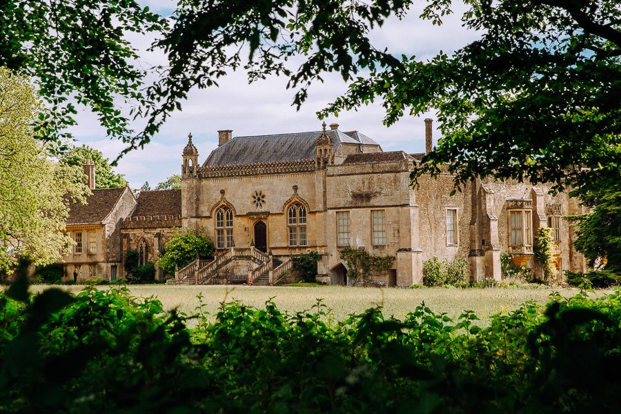 Lacock Abbey, a large ornate building through green trees